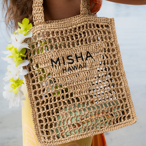 Woven bag with 'Misha Hawaii' branding held by a person against a blurred background
