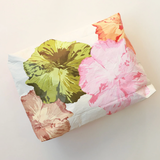 A square fabric pouch or small bag with a white base and a large watercolor-style floral print in pink, green, peach, and brown, photographed on a plain light background.